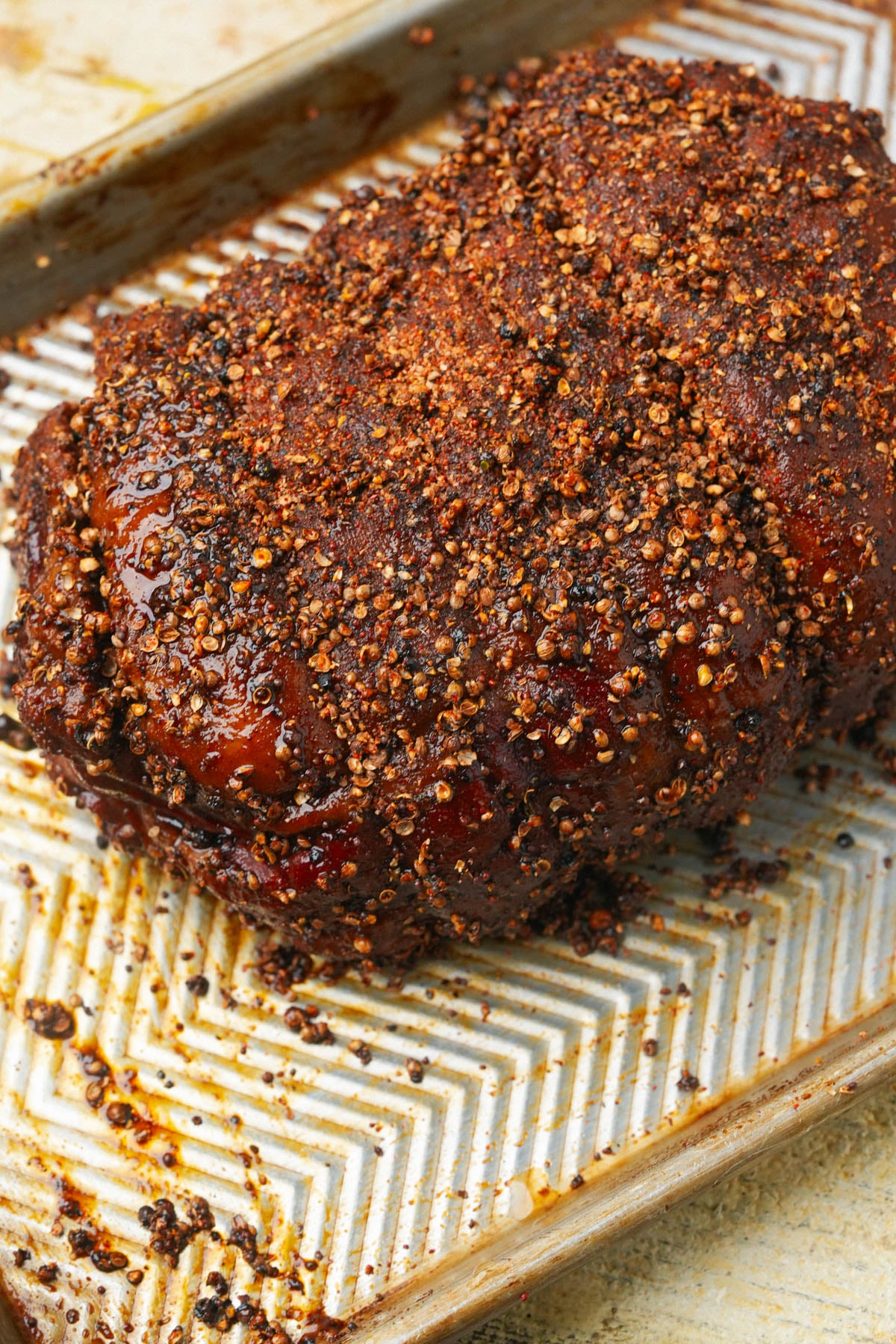 A large piece of roasted meat coated in a dark spice rub on a baking sheet.