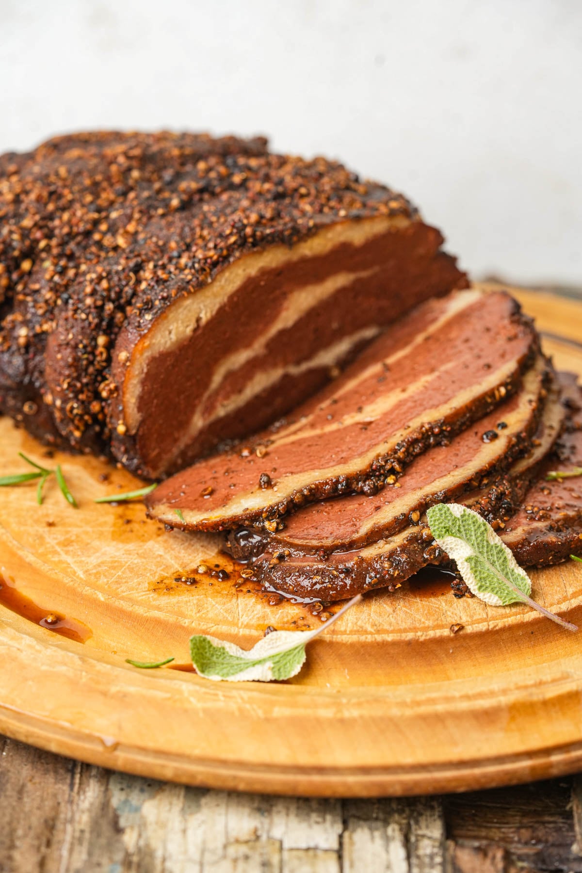 A sliced, spice-crusted roast on a wooden cutting board garnished with fresh sage.