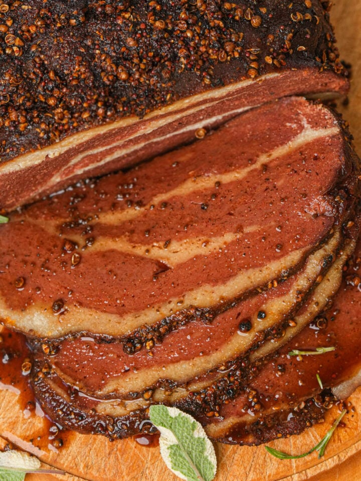 A sliced piece of pastrami with a heavily peppered crust on a wooden cutting board.