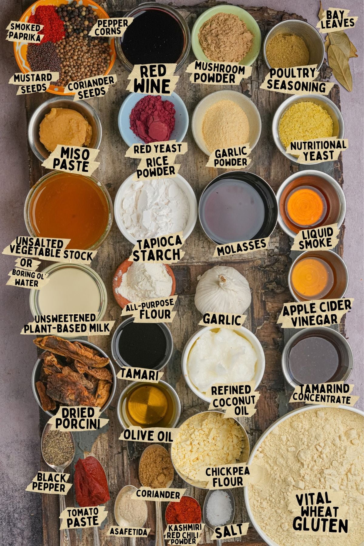 Top-down view of various ingredients in small bowls and piles, each labeled with its name, including miso paste, nutritional yeast, liquid smoke, coconut oil, and vital wheat gluten.
