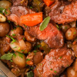 A vegan pot roast with chunks of seitan, pearl onions, baby potatoes, carrots, and fresh herbs in a rich, brown sauce.