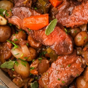 A vegan pot roast with chunks of seitan, pearl onions, baby potatoes, carrots, and fresh herbs in a rich, brown sauce.