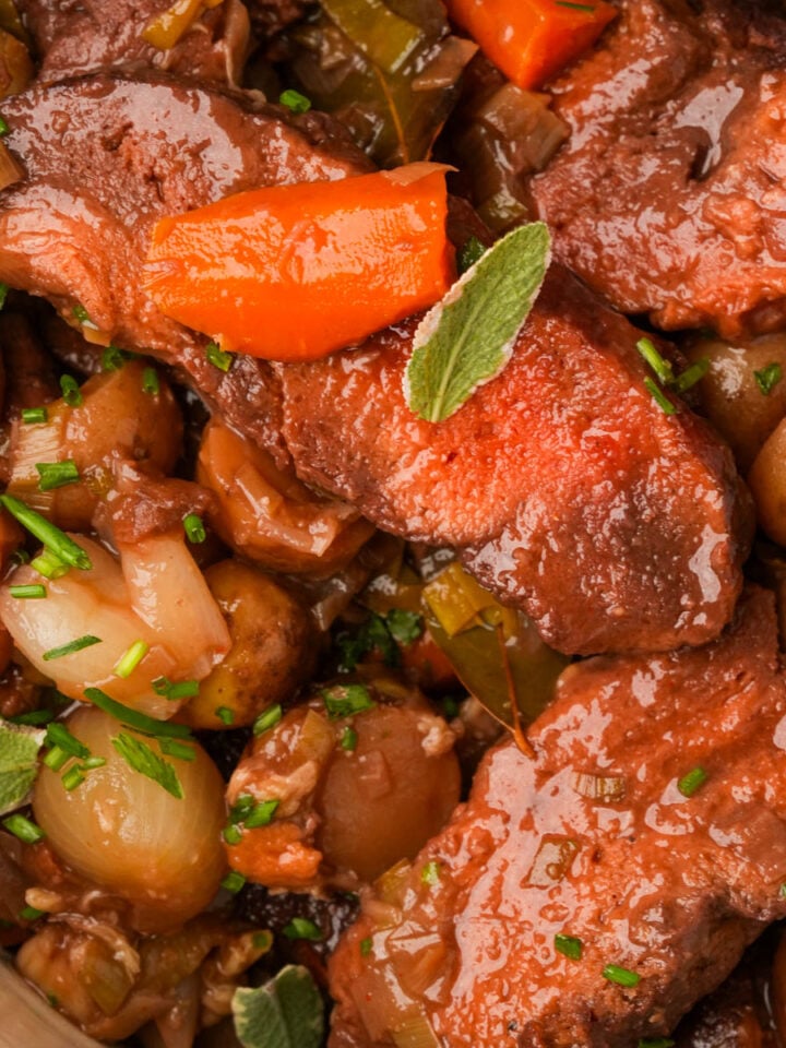 A vegan pot roast with chunks of seitan, pearl onions, baby potatoes, carrots, and fresh herbs in a rich, brown sauce.