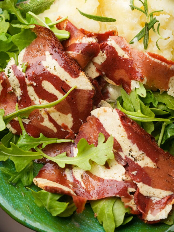 Slices of cured meat served over arugula with a side of mashed potatoes.