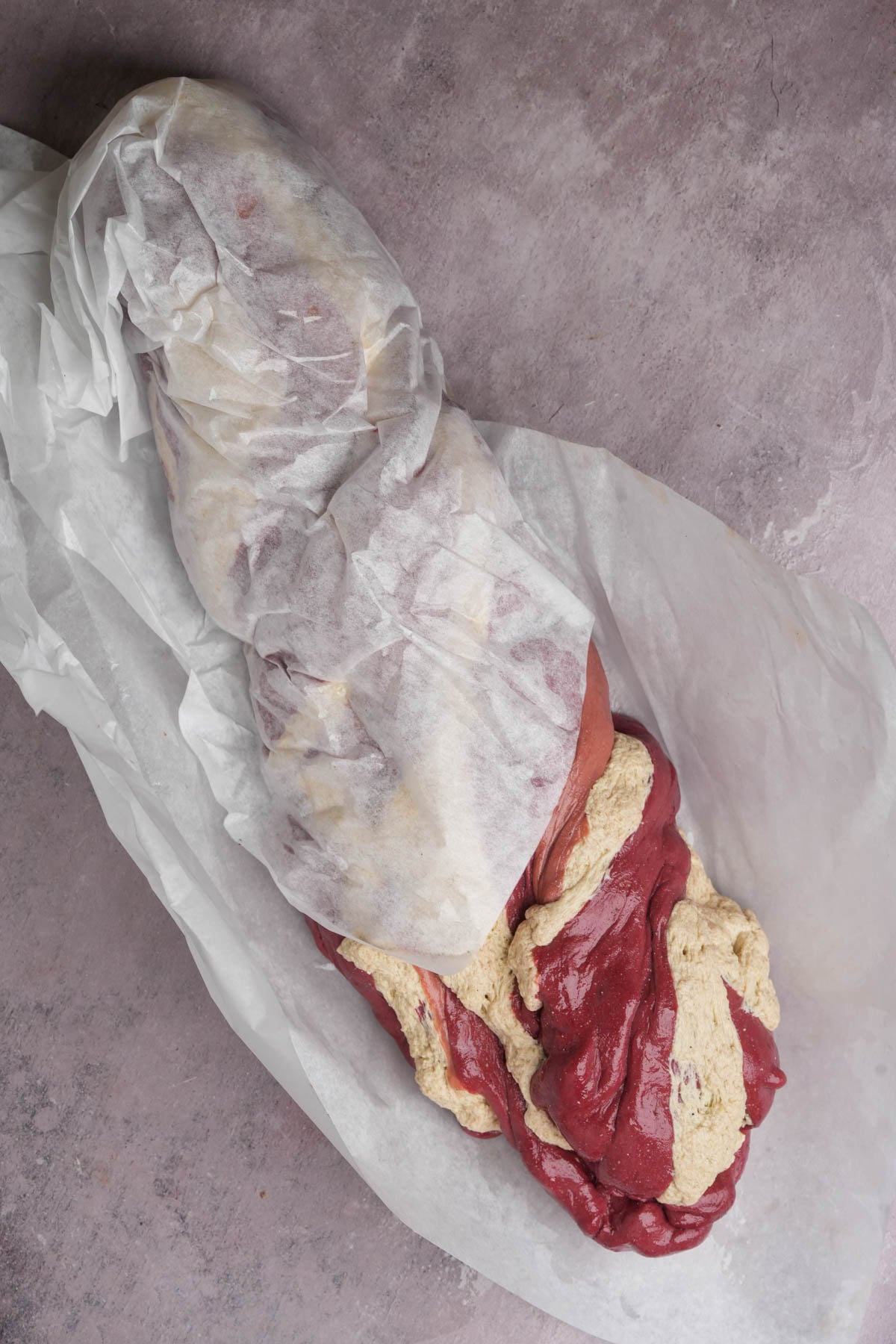 A raw beef roast partially wrapped in butcher paper and coated in a beige herb butter or rub.