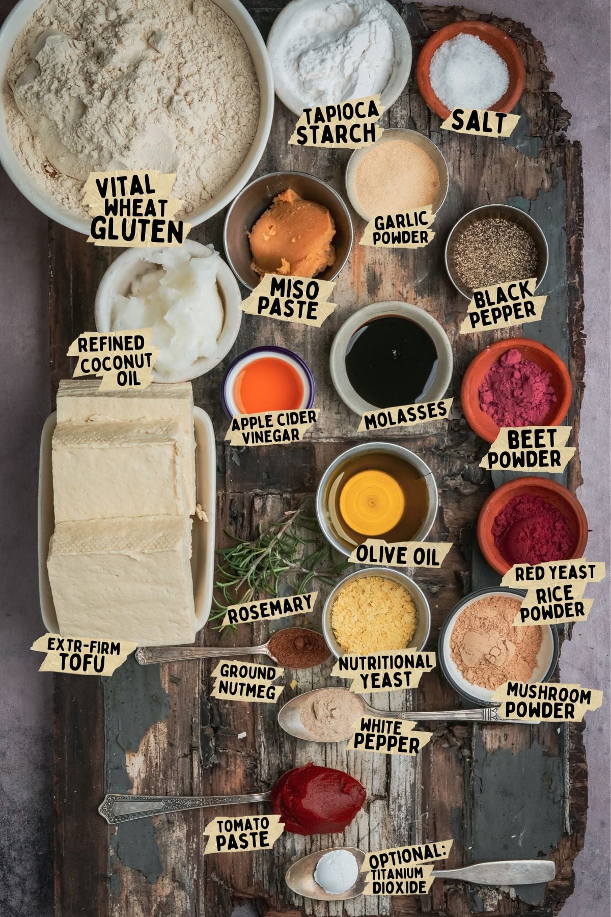 A flat-lay of recipe ingredients on a rustic wooden board, labeled with text pointers for items including vital wheat gluten, tofu, miso paste, various powders, oils, and seasonings.