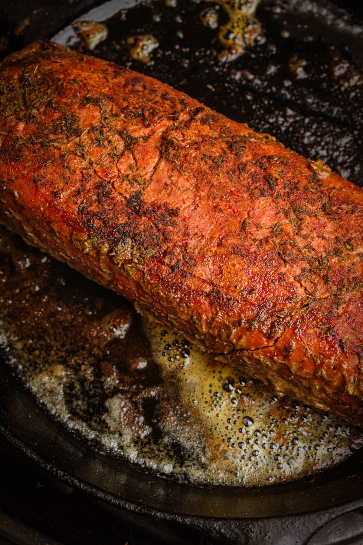 A seasoned, seared vegan roast beef cooking in a cast iron skillet with melted butter and juices bubbling around it.